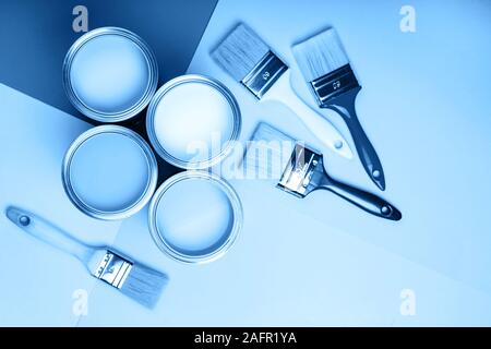 Quattro apri barattoli di vernice con spazzole su sfondo blu. Colore principale dell'anno 2020 in interni Foto Stock