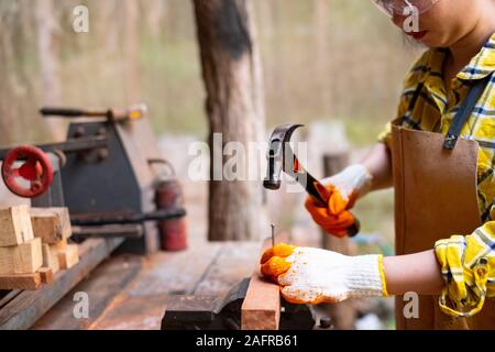 Le donne in piedi indossando generatore controllato shirt lavoratore del cantiere martellamento chiodo nella tavola di legno Foto Stock