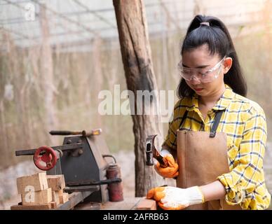 Le donne in piedi indossando generatore controllato shirt lavoratore del cantiere martellamento chiodo nella tavola di legno Foto Stock