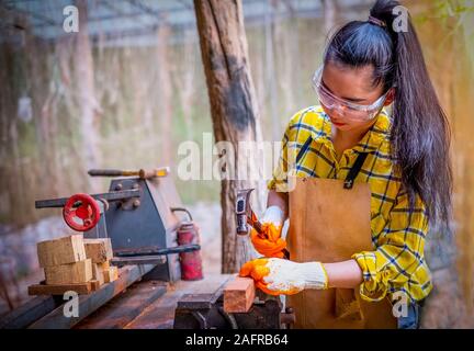 Le donne in piedi indossando generatore controllato shirt lavoratore del cantiere martellamento chiodo nella tavola di legno Foto Stock