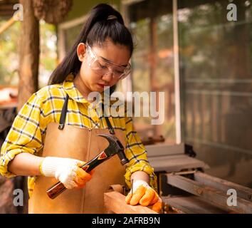 Le donne in piedi indossando generatore controllato shirt lavoratore del cantiere martellamento chiodo nella tavola di legno Foto Stock
