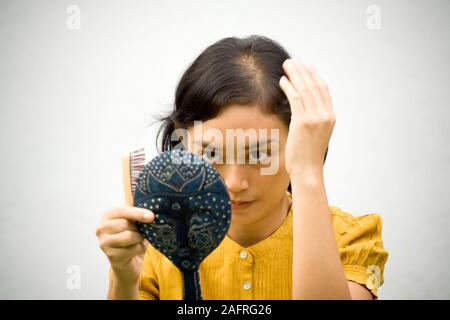 Piuttosto Southeast Asian giovane donna con capelli problema vestirsi con uno specchio antico e il pettine sulle mani Foto Stock