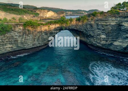 Elevato angolo di rotta spiaggia di Bali. Una roccia naturale archway con aqua verde baia d'acqua. Foto Stock