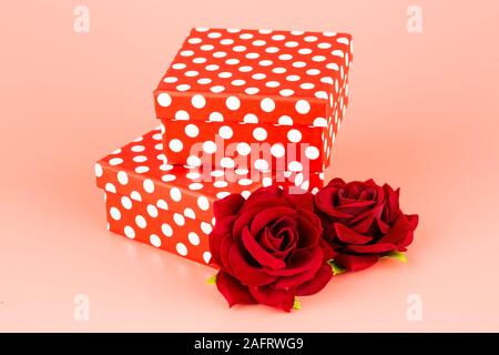 Due confezioni regalo e rose rosse isolato su sfondo rosa. Foto Stock