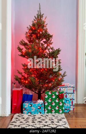 Piccolo albero di Natale decorato con luci rosse con regali e. Borse regalo sotto di esso in un soggiorno dell'appartamento Foto Stock