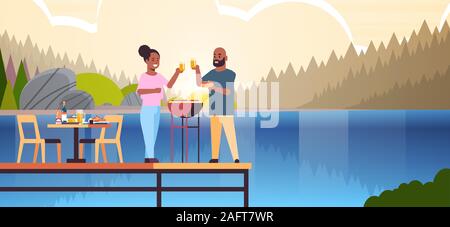 Coppia felice la preparazione di hot dog sul grill e di bere succo di frutta african american uomo donna in amore in piedi sul molo in legno avente il concetto di picnic in riva al fiume sullo sfondo del paesaggio per tutta la lunghezza orizzontale illustrazione vettoriale Illustrazione Vettoriale