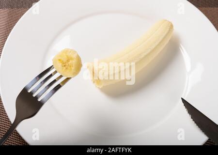 Vista superiore a mangiare una banana fresche con la forchetta e coltello Foto Stock