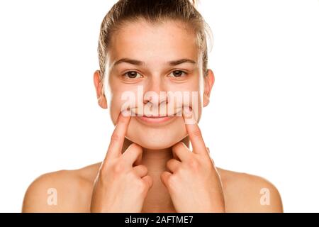 Giovane donna forzando il suo sorriso con le dita su sfondo bianco Foto Stock