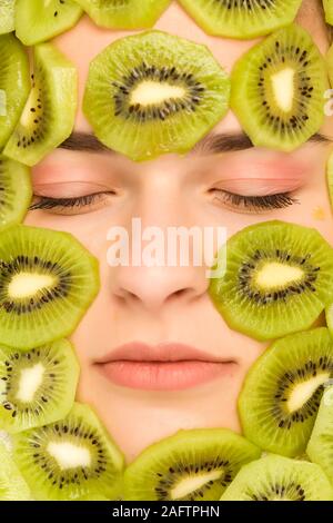 Giovane bella donna in posa con fette di kiwi sul suo viso Foto Stock