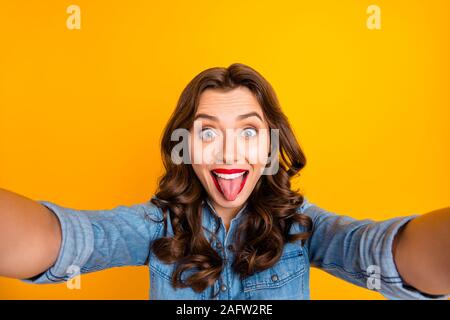 Foto di ricci allegro ondulata affascinante ragazza carina con la lingua fuori tenendo selfie giocoso isolato su giallo vivido colore di sfondo Foto Stock