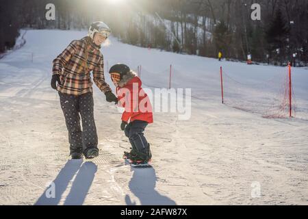 La Madre insegna il figlio lo snowboard. Attività per bambini in inverno. Bambini sport invernali. Stile di vita Foto Stock