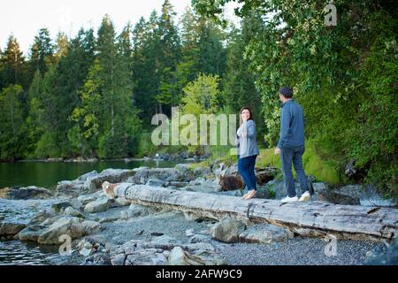 Coppia felice camminando sul registro caduti a Lakeside nei boschi, Mill Bay, British Columbia, Canada Foto Stock