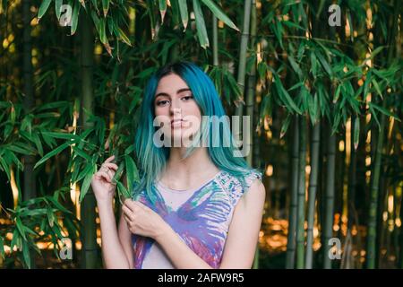 Ritratto di giovane donna con capelli blu in piedi sotto gli alberi di bambù Foto Stock