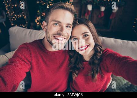 Foto di affascinante giovane trascorrere il Natale insieme rendendo selfies in ghirlanda decorata sala luci vicino newyear tree indoor indossare pullover rosso Foto Stock