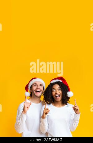 Multirazziale giovane indossando cappelli di Babbo Natale rivolti verso l'alto in uno spazio di copia Foto Stock