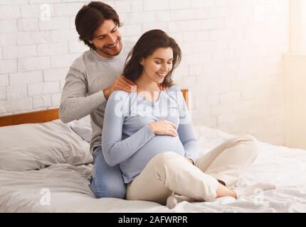 Amorevole marito rendendo massaggio alla schiena per il suo felice moglie incinta Foto Stock