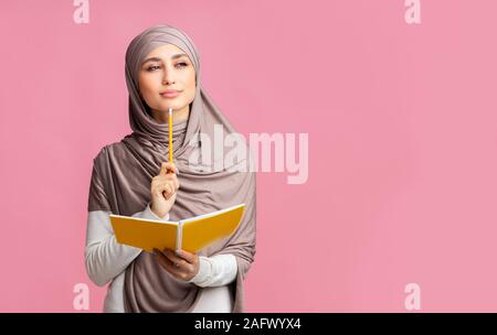 Malinconici ragazzina musulmana tenendo premuto il Blocco note e penna, pensando a qualcosa di Foto Stock