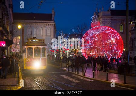 Lisbona, Portogallo - circa dicembre, 2019: un tradizionale vecchio tram passa davanti le decorazioni di Natale Illuminazione di Luiz cammei piazza di sera Foto Stock