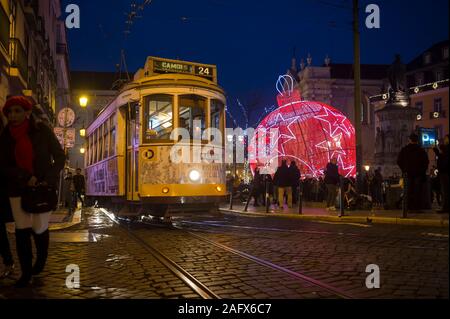 Lisbona, Portogallo - circa dicembre, 2019: un tradizionale vecchio tram passa davanti le decorazioni di Natale Illuminazione di Luiz cammei piazza di sera Foto Stock
