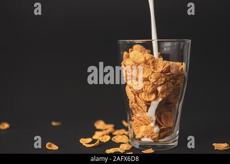 cornflakes con latte in un vetro trasparente su fondo nero Foto Stock