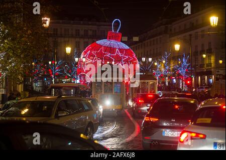 Lisbona, Portogallo - circa dicembre, 2019: un tradizionale vecchio tram bloccato nel traffico occupato nella parte anteriore delle decorazioni di Natale Illuminazione di Luiz cammei sq Foto Stock