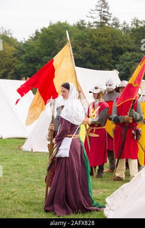 Donna vestita in tipico costume medievale con i soldati a una rievocazione camp Foto Stock