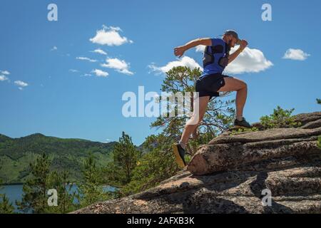 Runner arrampicata roccia. L'atleta corre sulle rocce in montagna. Outdoor trail running. Uomo in blu t-shirt e pantaloncini neri della formazione Foto Stock