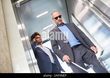 Cieco con gli occhiali e la canna da zucchero in ascensore in ufficio business Foto Stock
