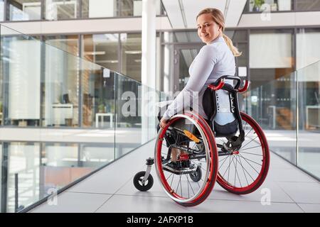 Sorridente giovane donna in sedia a rotelle in azienda per il concetto di inclusione Foto Stock
