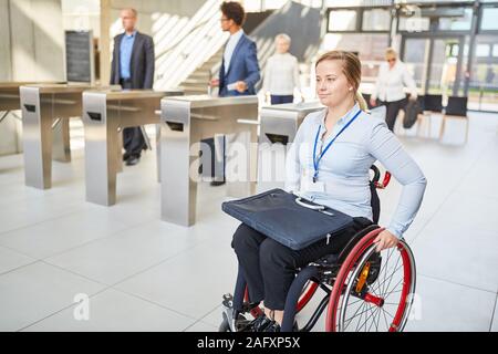 Imprenditrice in una sedia a rotelle accessibile oltre il cancello di sicurezza in ufficio Foto Stock