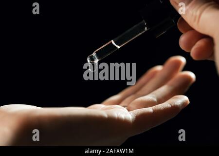 La cura della pelle e il trattamento - donna gocce di olio in una mano con pipetta su sfondo nero Foto Stock