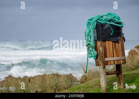 Coruna / Spagna - 15 dicembre 2019: verde aggrovigliati di corda in un cestino di legno può sulla cima di una scogliera che si affaccia sull'Oceano Atlantico Foto Stock