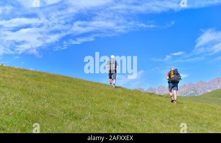 Gli escursionisti salendo una collina erbosa in montagna alpina sotto il cielo blu Foto Stock