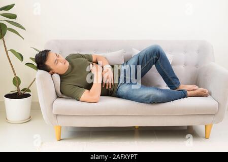 Uomo che impugnano il suo stomaco da dolore acuto, sdraiato sul lettino Foto Stock