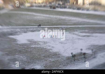 Tilt Shift vista da lontano non identificato di adulti e bambini a camminare in una grande pozza ricoperta di neve e ghiaccio nella piazza della città Foto Stock