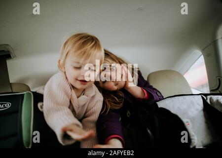 Sorelle sporgendoti sul sedile posteriore della vettura insieme Foto Stock