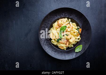 La pasta italiana Le fettuccine in una salsa cremosa con gamberi su una piastra nera, vista dall'alto Foto Stock