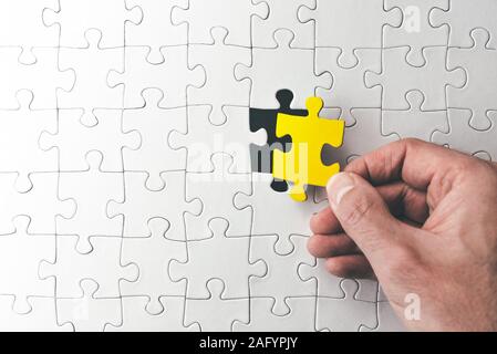 Vista superiore della mano che tiene la scorsa corrispondente pezzo di puzzle a destra prima del completamento Foto Stock