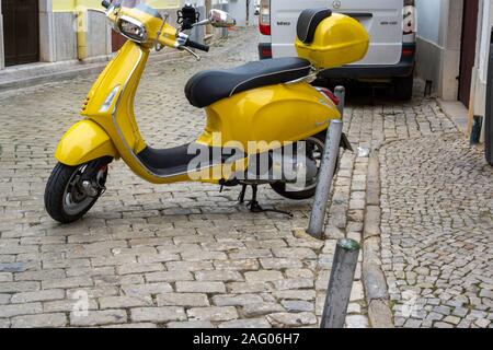 .Un giallo Vespa scooter parcheggiato su una mattonella lapidato road a Loulé, Portogallo Foto Stock