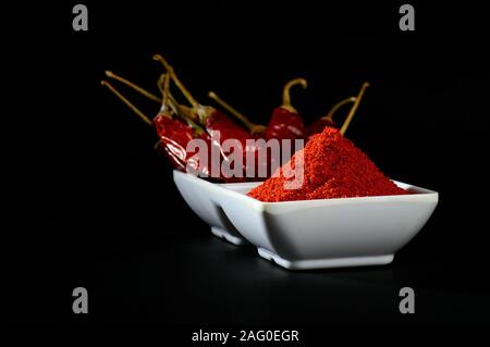 Peperoncino in polvere con peperoncino rosso in piastra bianca, essiccati peperoncini rossi su sfondo nero Foto Stock