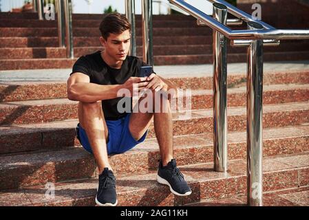 Giovane ragazzo in abiti casual siede su per le scale con lo smartphone in mani Foto Stock