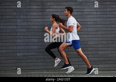Vista laterale. L uomo e la donna hanno il giorno di fitness e in esecuzione nella città di giorno vicino a un muro di mattoni Foto Stock