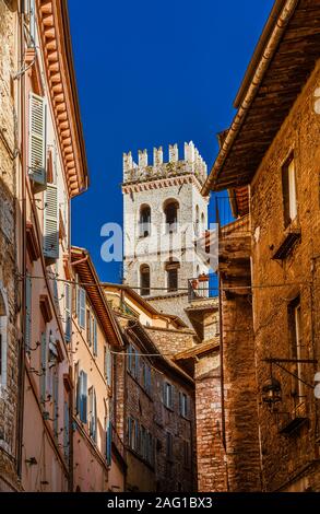 Vista di Assisi centro storico incantevole con la medievale Torre del Popolo (), un punto di riferimento della città, da una stretta viuzza Foto Stock