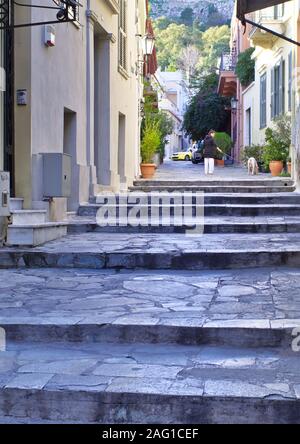 La Plaka, Atene / Grecia - Dicembre 06, 2019: gradini di pietra nella città vecchia sotto la collina dell'Acropoli. Donna con cane in background. Foto Stock