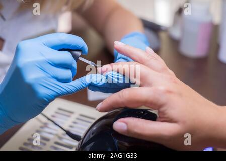 Capitano donna manicure. La ragazza non manicure in un salone di bellezza. Sotto una lampada da tavolo, in un ufficio, closeup mani e unghie di verniciatura Foto Stock