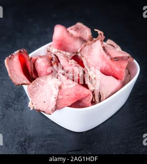 Porzione di Roastbeef (tagliata a fette; messa a fuoco selettiva) su una lastra di ardesia Foto Stock