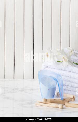 Plastica blu, bicchiere di misurazione con detergente, stack di bianco asciugamani di spugna, white orchid fiore e clothespins in legno sono su un piano di marmo contro Foto Stock