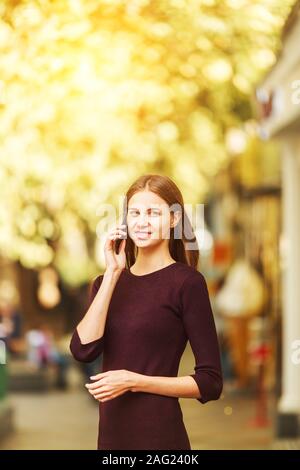 Donna che indossa abiti di borgogna texting su smart phone a piedi in strada in una giornata di sole Foto Stock