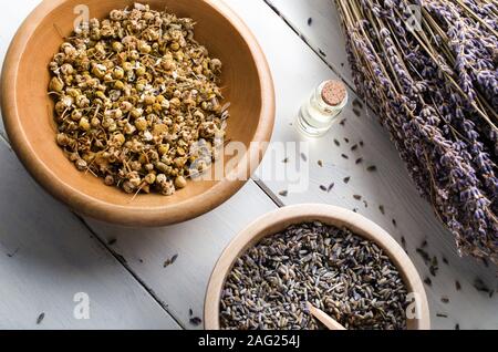 Overhead angolato colpo di erbe essiccate e olio essenziale. Include ciotole di legno di camomilla e lavanda con legato un mazzo di fiori con gambo alla sid Foto Stock