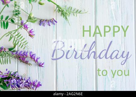 L'iscrizione Buon Compleanno di lilla fiori selvatici in una curva di sfondo in legno in stile rkstik. Auguri di compleanno design della scheda Foto Stock